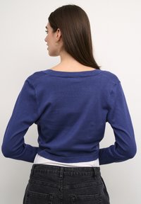 Cropped purple knit sweater with long sleeves and a wide neckline, paired with high-waisted black jeans featuring back pockets.