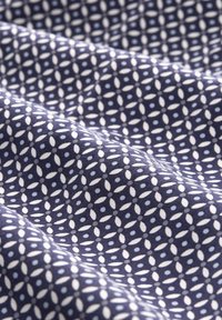 Tissu marine avec un motif géométrique de petits ovales blancs et de points bleu clair, présenté avec des plis doux et des détails de texture.