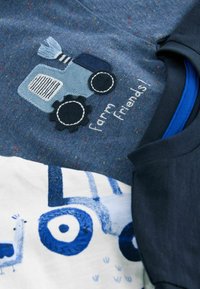Zwei T-Shirts: eines in Marineblau mit einem blauen gestickten Traktor und dem Schriftzug "Farmfreunde"; das andere ist weiß mit blauen Traktor- und Vogelmotiven. Weicher Baumwollstoff.