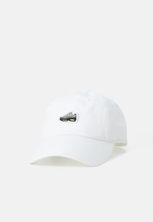 White cotton cap with a curved brim, featuring a black and green embroidered sneaker patch on the front.