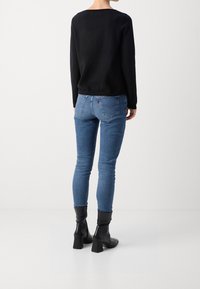 Czarna bluzka z długim rękawem, zestawiona z dopasowanymi niebieskimi dżinsami i czarnymi botkami na obcasie. Gładkie tekstury i prosty design, minimalne ozdoby.