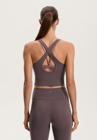 Fialový športový crop top s priečne prekríženými ramienkami a vyrezaným detailom. Hladká textúra a priliehavý dizajn, spárovaný s terasovými legínami s vysokým pásom.