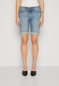 Vaaleansiniset farkkushortsit, joissa on käännetyt lahkeet, viiden taskun malli ja istuva siluetti. Yhdistetty mustiin, teräväkärkisiin kenkiin.