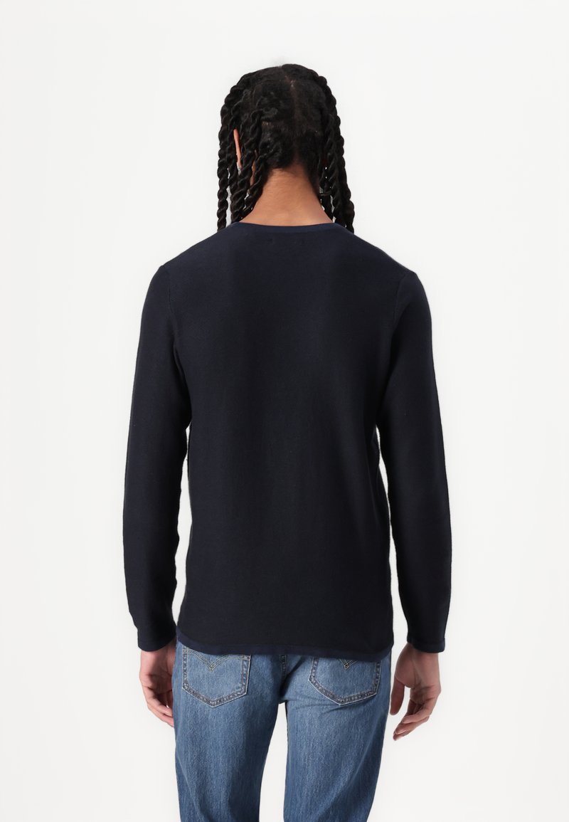 Marineblauer gestrickter Pullover mit langen Ärmeln, rundem Halsausschnitt und glatter Textur, kombiniert mit hellblauen Jeans.