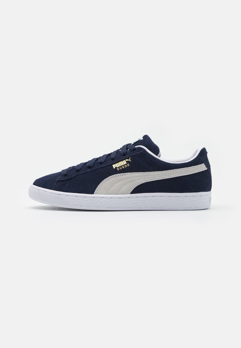 Baskets Puma en daim bleu marine avec semelle blanche et bande latérale grise, dotées de lacets bleu marine et du logo "Puma Suede" doré sur le côté.