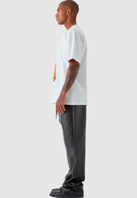Hvit oversized t-skjorte med grafisk design, parret med svarte faux skinnbukser. Modellen står sidelengs og viser frem den avslappede passformen og designet.