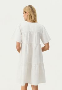 Vit, lager-på-lager klänning med korta ärmar, med texturerad tyg och sammanknippade sömmar i ryggen. Enkel, avslappnad silhuett.