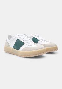 Sneaker bianchi con striscia in suede verde, tomaia in pelle liscia e suole in gomma. Presentano punte arrotondate e dettagli testurizzati sulla gomma.