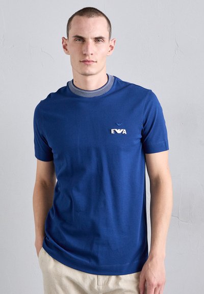 T-shirt bleu à manches courtes en coton, avec un col côtelé à rayures blanches et un petit logo brodé sur la poitrine.