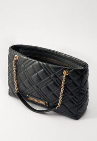 Borsa a tracolla nera trapuntata con catena dorata e manici in pelle. Presenta una placca con logo metallico e un compartimento interno con zip.