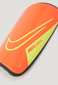 Parastinchi arancioni e gialli con una superficie lucida, caratterizzati da un design diagonale, bordi cuciti e un bordo nero. Presente il logo "Mercurial".