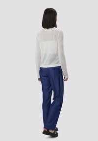 Suéter blanco de punto de malla con mangas largas y cuello redondo, combinado con pantalones de corte holgado en azul marino y sandalias negras.