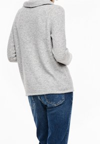 Maglione grigio lavorato a maglia con colletto, caratterizzato da una vestibilità comoda e dettagli cuciti. Abbinato a jeans in denim blu con design delle tasche.