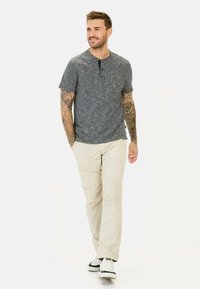 Szary melanżowy t-shirt z krótkim rękawem w stylu henley z zapięciem na guziki, połączony z jasnobeżowymi spodniami i białymi trampkami, o luźnym kroju.