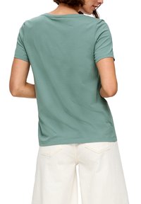 Zielona krótko rękawowa koszulka wykonana z miękkiego materiału, o luźnym kroju i okrągłym dekolcie, zestawiona z białymi szerokimi spodniami.