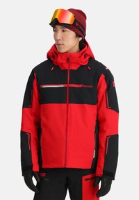 Rote und schwarze Skijacke mit durchgehendem Reißverschluss, verstellbarer Kapuze und kontrastierenden Farbblöcken. Verfügt über reflektierende Akzente und verstärkte Bündchen.