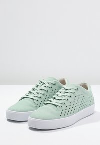 Světle mátově zelené tenisky s semišovou texturou, s perforacemi po stranách, kulatou bílou gumovou podrážkou a odpovídajícím šněrováním.