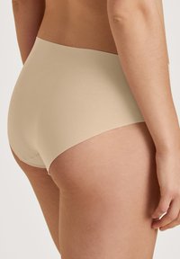 Beige hoge taille slip met een zachte textuur, minimale naden en een elastische tailleband, ontworpen voor comfort en bedekking.