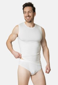 White sleeveless tank top made of textured material, fitted design, paired with white briefs, model holding shirt, displaying smooth fabric.