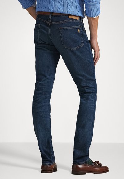 Σκούρο μπλε βαμβακερά τζιν με εφαρμογή slim fit, που διαθέτουν πίσω τσέπες, ραφές αντίθεσης και δερμάτινη ετικέτα στη μέση.