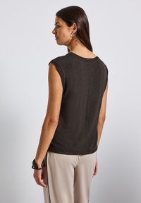 Tmavě šedý bezrukávový top s kulatým výstřihem a hladkým povrchem, kombinovaný se světlými béžovými kalhotami s černými bočními pruhy.