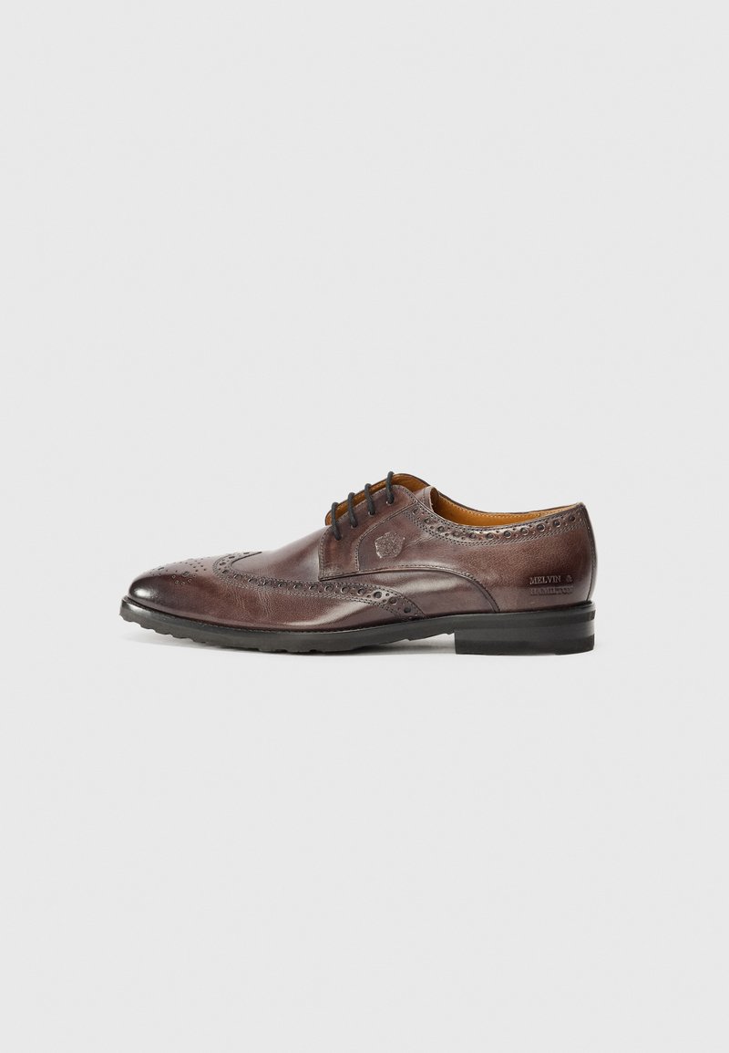 Brune lærdressko med brogue-detaljer, spiss tå og en lett hæl. Snøring med subtil merkevare på siden.