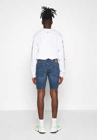 Shorts de mezclilla en un tono azul medio, con un dobladillo deshilachado. Combinados con una camisa blanca de manga larga y zapatillas verde claro.