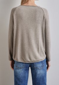 Jasnoszary, miękki sweter z długimi rękawami i zaokrąglonym dekoltem, zestawiony z niebieskimi dżinsami z tylnymi kieszeniami i wyblakłym przodem.