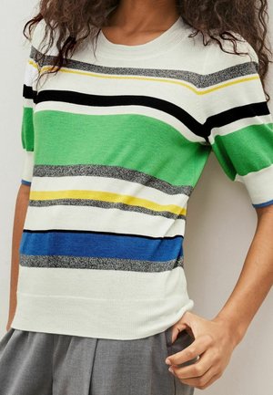 Person wearing a white short-sleeve sweater with horizontal green, blue, black, yellow, and gray stripes, paired with gray pants.