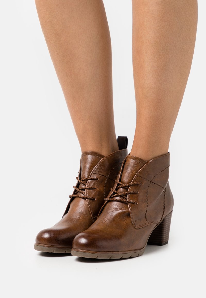 Braune Lederstiefeletten mit Schnürdesign, mit einer geschwungenen Schnittführung, strukturierten Oberflächen und einem gestapelten Absatz.