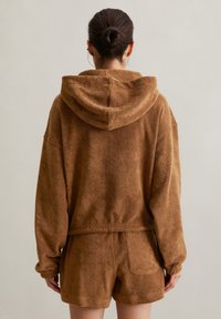 Haut à capuche en polaire marron avec une coupe ample, associé à un short en polaire marron. Le tissu semble doux et texturé.