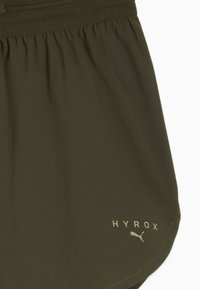 Oliivrohelised spordilühikesed püksid, millel on elastne vöökoht ja lahtine istuvus. Sisaldab heledas toonis trükitud "HYROX" logo ja Puma kassi sümbolit.