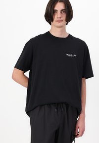 Black cotton t-shirt with short sleeves, crew neckline, and a small white logo on the left chest. Paired with black drawstring shorts.