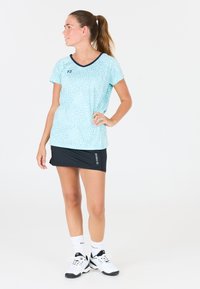 Ljusblå träningsblus med en texturerad leoprint, parat med en svart kjol. Outfiten inkluderar vita skor och strumpor med logodetaljer.