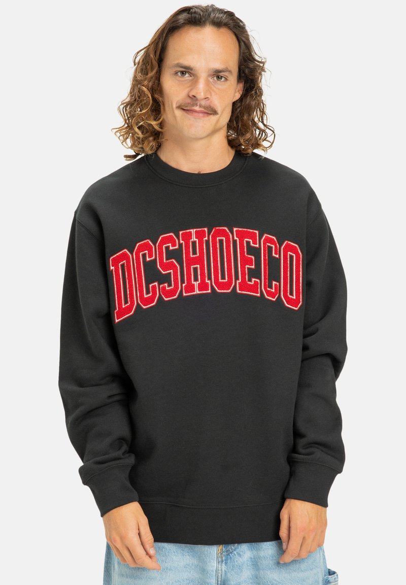 Čierna mikina s výrazným červeným retro štýlovým logom "DCSHOECO" na hrudi, vyrobená z mäkkej látky s rebrovanými manžetami a lemom.