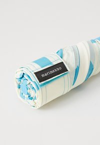 Umbrella rolled up with a blue and white striped fabric and a black label. The handle features a blue button. Textured fabric with a smooth finish.