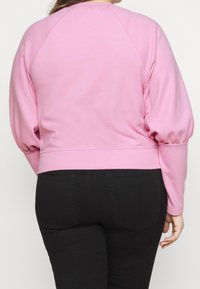 Różowy krótkie bluza z długimi bufiastymi rękawami i okrągłym dekoltem. Miękka tkanina o gładkiej fakturze, zestawiona z czarnymi, dopasowanymi dżinsami.