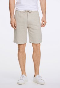 Shorts en mélange de lin beige avec une taille à cordon, des poches latérales et une coupe décontractée, associés à des baskets blanches.