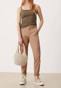 Olivgrön spaghetti-strap linne, beige avslappnade byxor, krämfärgad vävd handväska och beige högstövelsneakers med snörning.