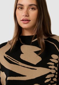 Maglione nero con motivi astratti beige, caratterizzato da un collo alto e una morbida texture a maglia. Vista ravvicinata che mette in evidenza i dettagli di design.