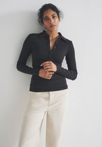 Black long-sleeve polo shirt with a buttoned placket and ribbed texture, paired with cream-colored wide-leg pants. Simple design, elegant fit.