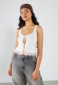 Vit kort klänningstopp med spetsdetaljer, med en knytframsdesign. Kombinerad med högmidjade denimjeans med gradient från ljus till mörk.