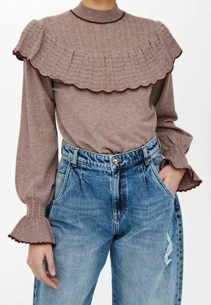 Haut en tricot brun avec un col à volants texturé, manches longues avec des poignets évasés ; associé à un jean en denim bleu clair taille haute avec des détails effilochés.