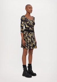 Black dress with a floral yellow and white pattern, featuring a fitted top, long sleeves, and a pleated skirt, paired with black combat boots.