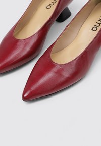 Escarpins en cuir bordeaux avec un bout pointu et un petit talon carré ; texture lisse avec un design minimaliste et un logo de marque à l'intérieur.