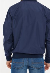 Marinblå bomberjacka med ett glatt, lätt tyg, ribbade ärmslut och elastisk midja. Utstrålar en enkel, klassisk design.