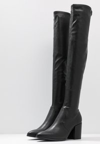 Black, knee-high, faux leather boots with a pointed toe and chunky block heel, featuring a side zipper and smooth texture.