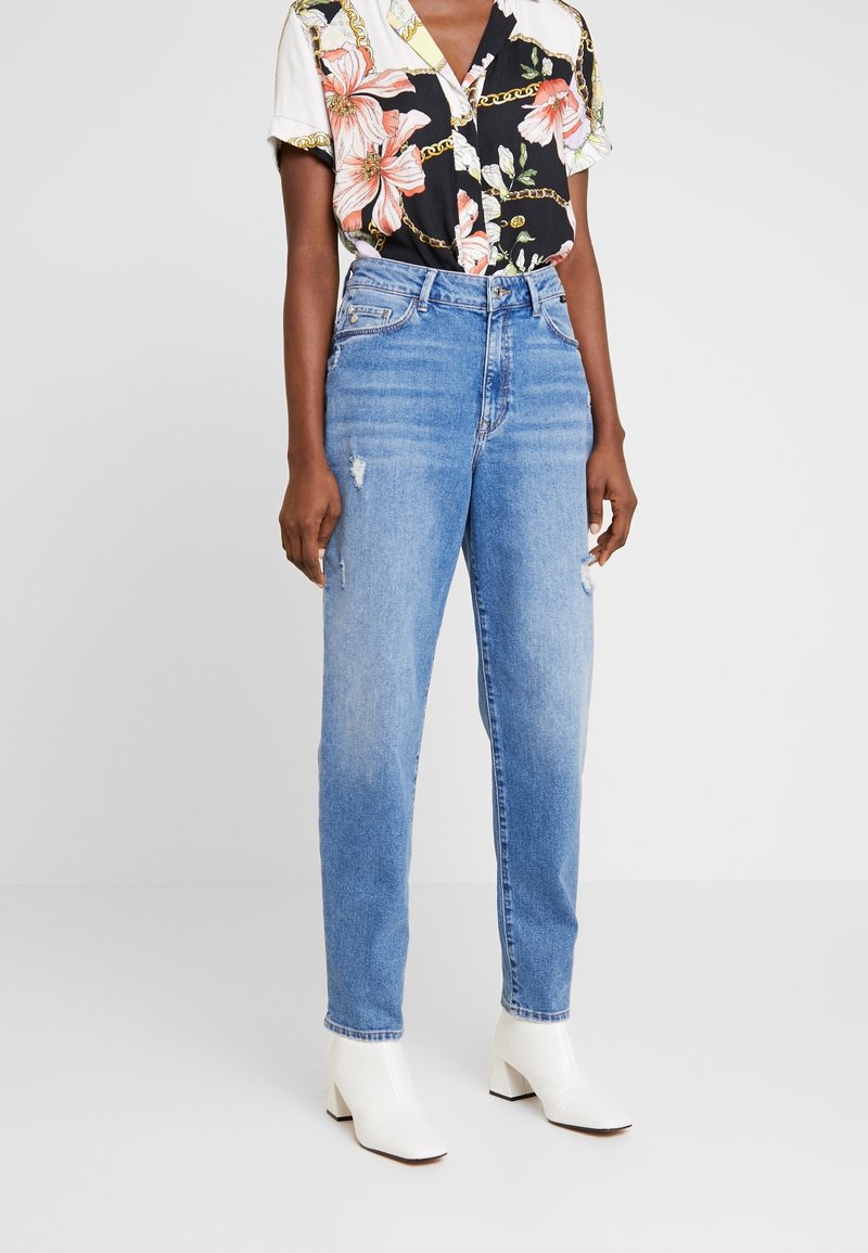 Svart blommig skjorta med kedjemönster, kombinerad med ljusblå, urtvättade högmidjade jeans och vita ankelboots.