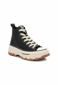 Zapatilla alta negra con cordones crema, puntera de goma, parte superior de cuero texturizado, suela gruesa blanca y marrón, y un lazo en el talón.