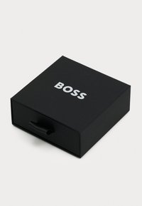 Boîte rectangulaire noire avec une finition mate, portant "BOSS" en texte blanc gras sur le couvercle et une languette noire à l'avant.